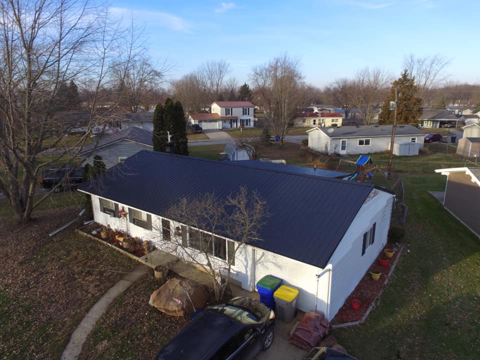 Aerial view of a home with a newly installed steel roof by Affordable Roofing in late December, with bare winter trees